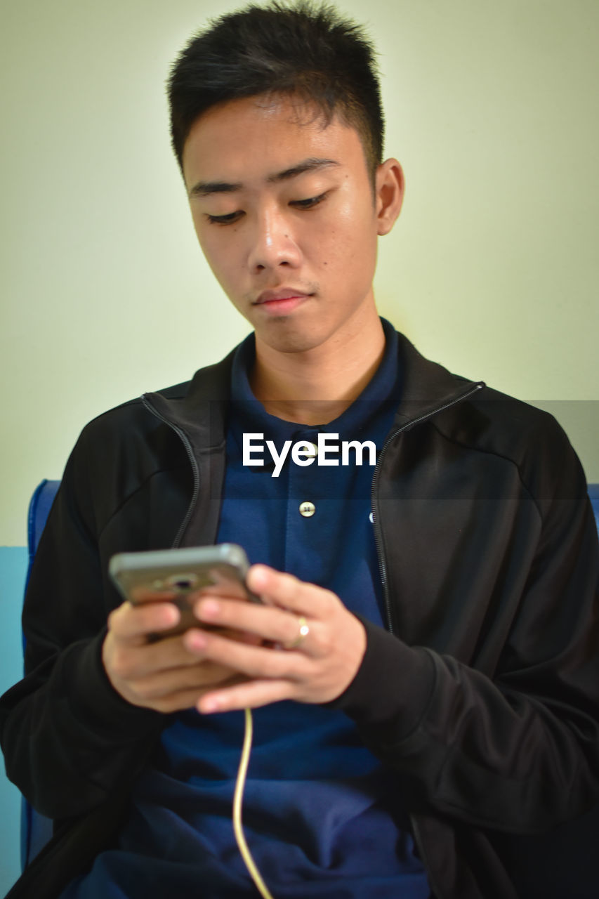 Young man using mobile phone against wall