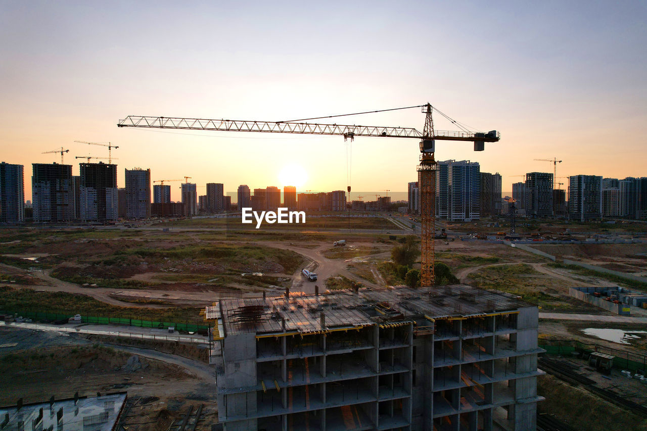 CONSTRUCTION SITE BY BUILDINGS AGAINST SKY AT SUNSET