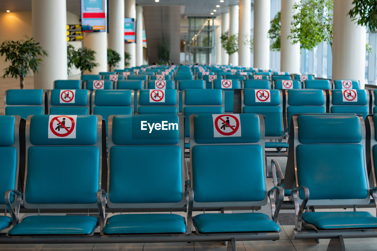 Airport during coronavirus pandemic. social distancing. empty blue chairs with a no-sitting sign