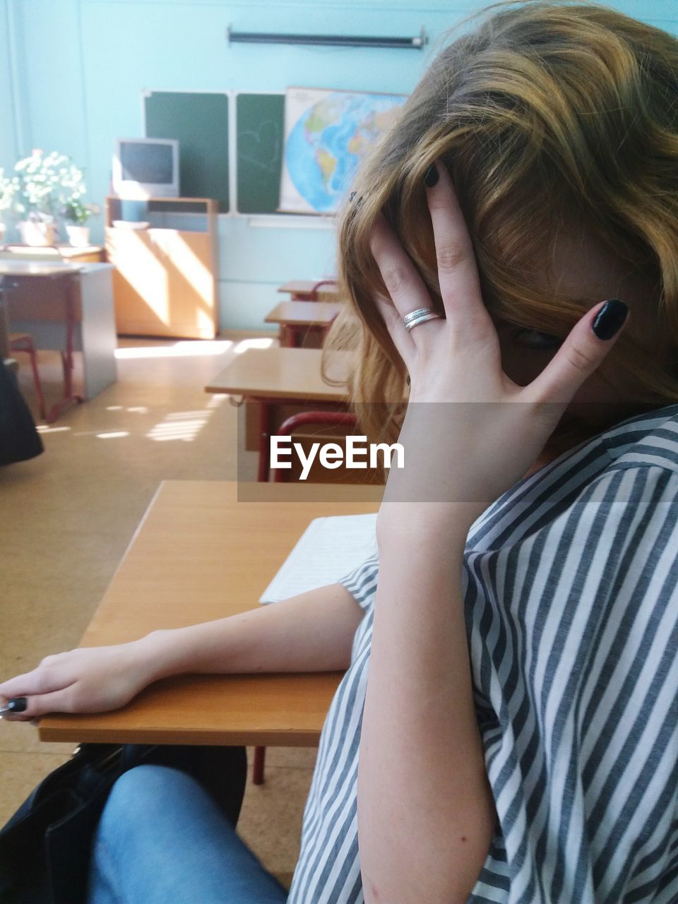 Woman with hands covering face sitting at desk in classroom