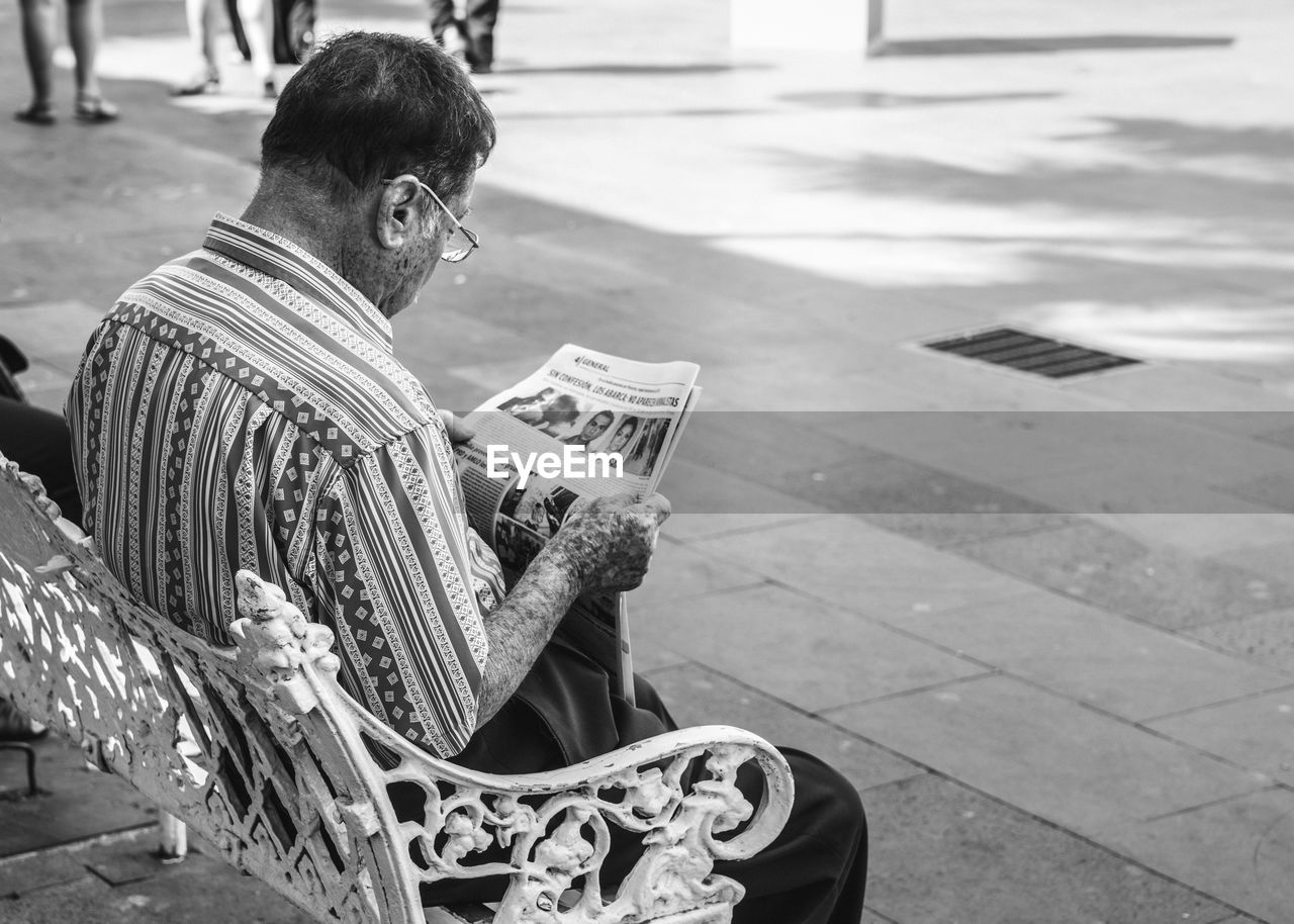 SIDE VIEW OF MAN SITTING ON STREET AGAINST CITY