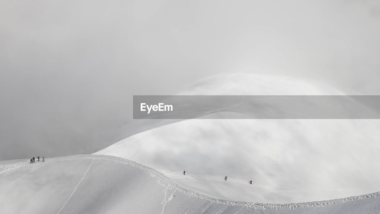 Scenic view of snowcapped mountain with mountaineers against sky