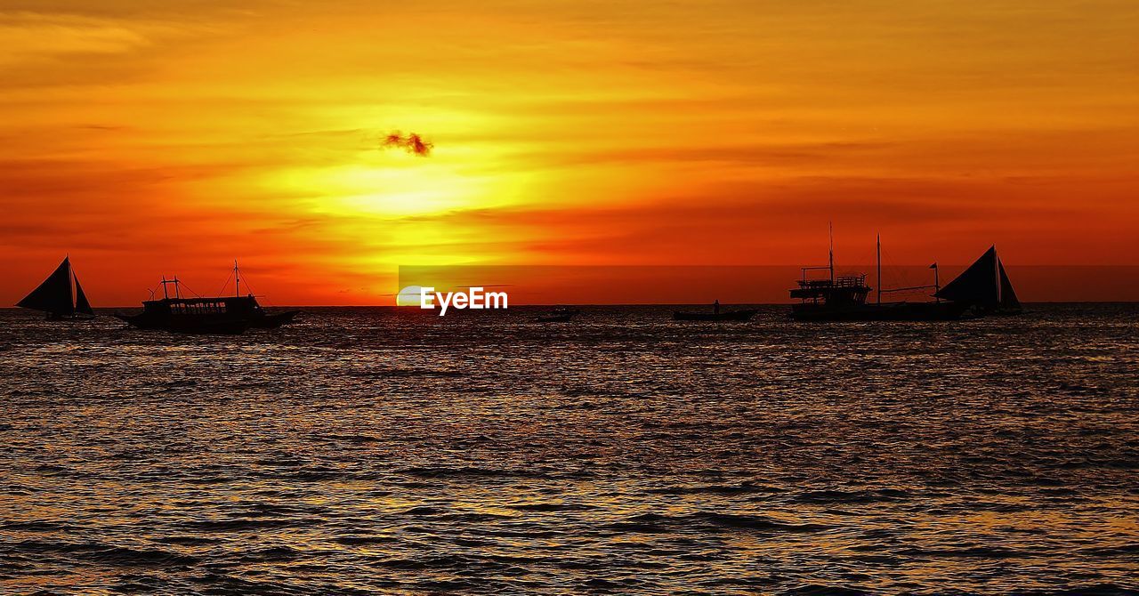 Silhouette boats sailing in sea against orange sky