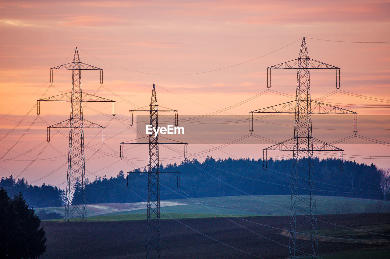 Electricity pylon on landscape against sky at sunset