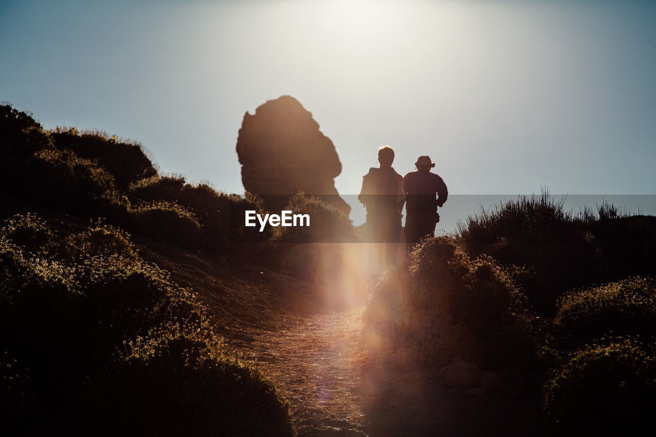 People walking on mountain against sky during sunset