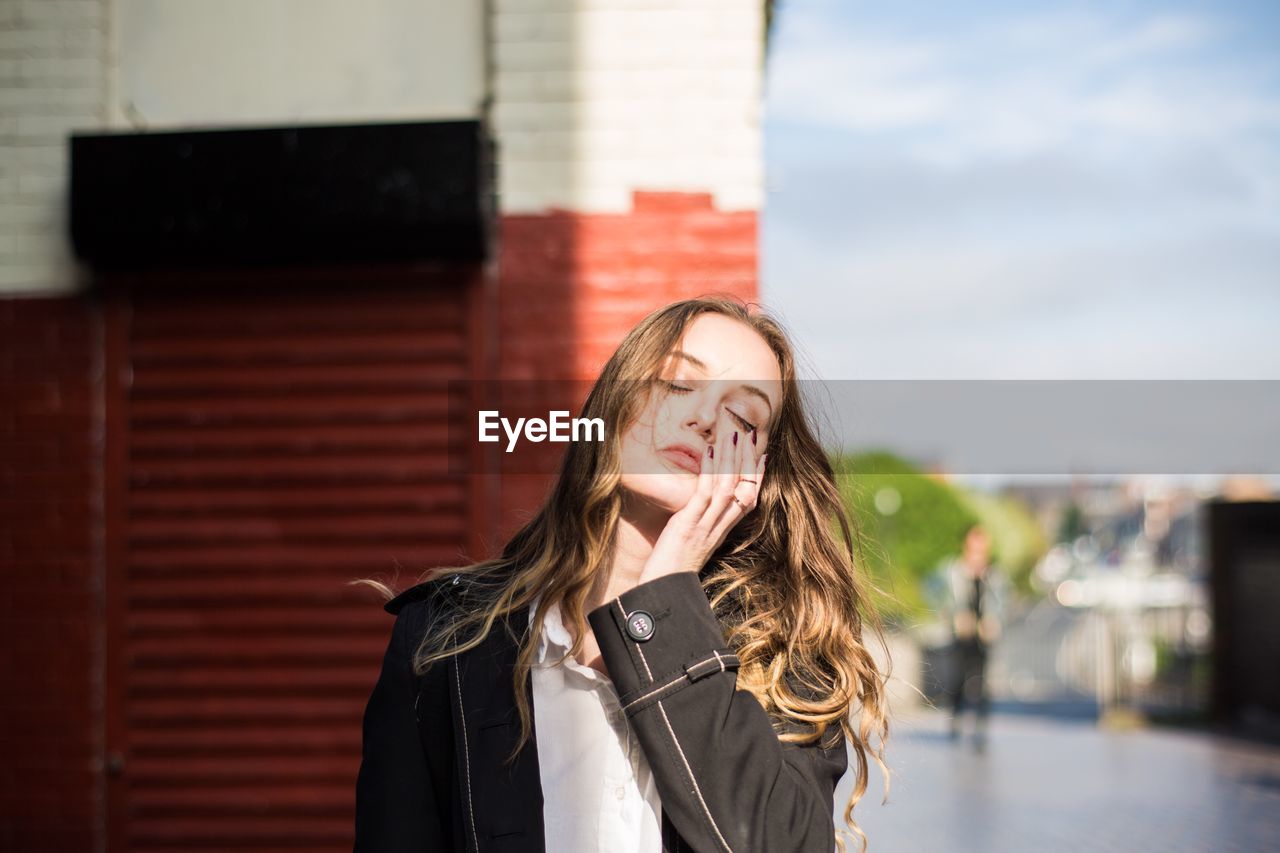 Young woman with eyes closed standing against wall