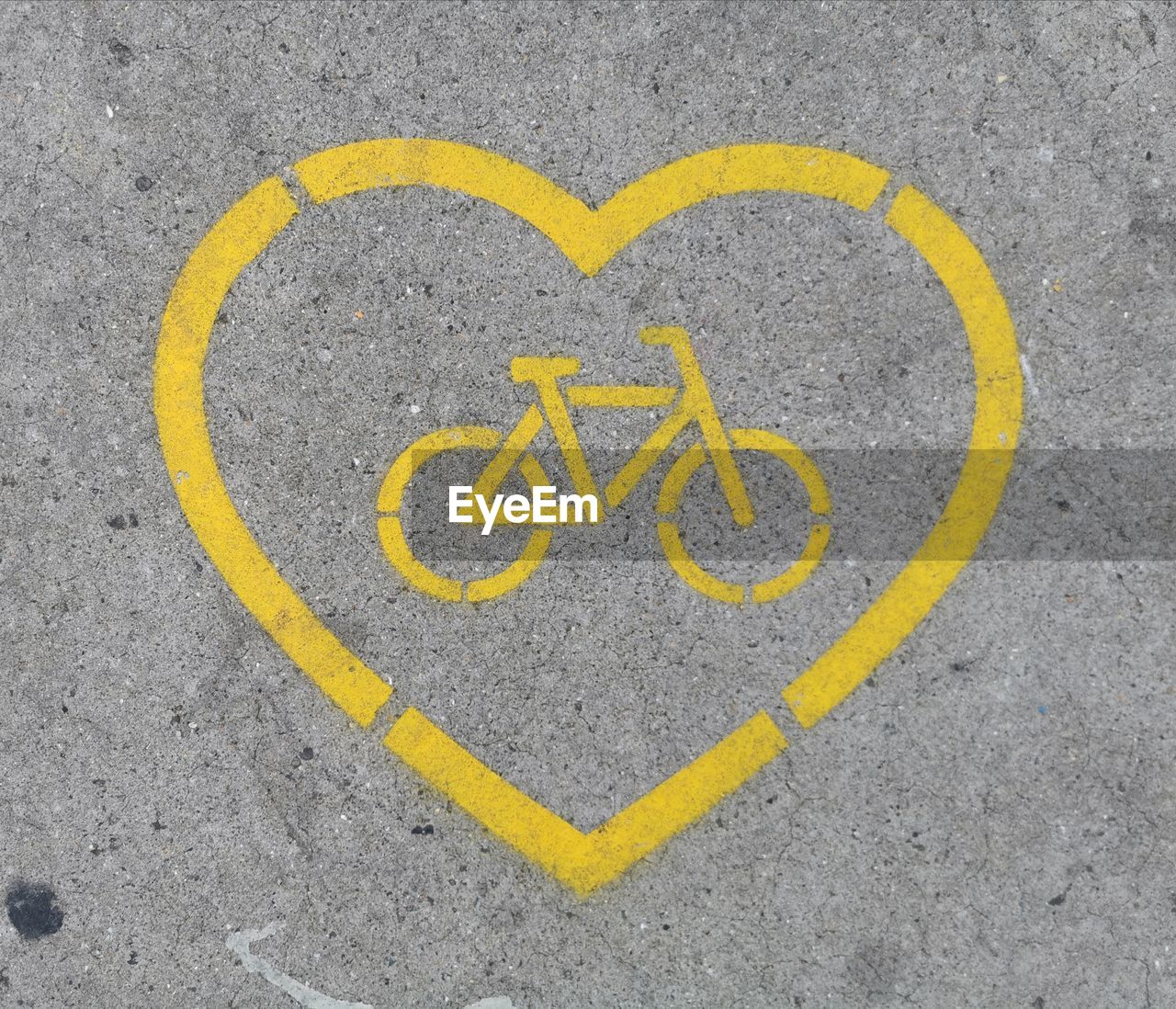 Directly above shot of yellow heart shape with bicycle lane marking on road