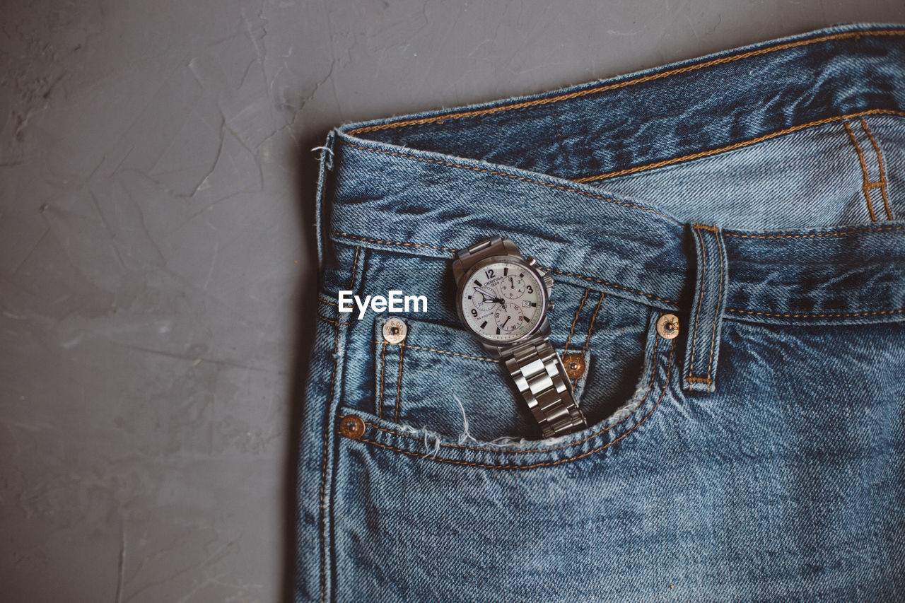 High angle view of wristwatch in jeans pocket on table