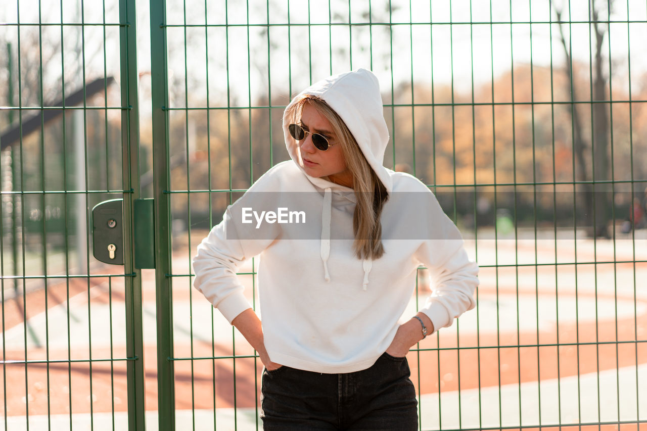 Young woman wearing sunglasses while standing against metal gate