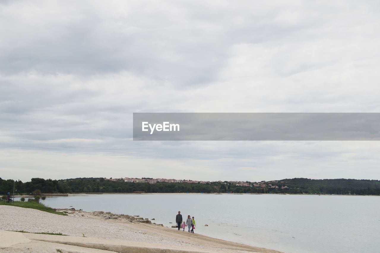 Family walking at beach against cloudy sky