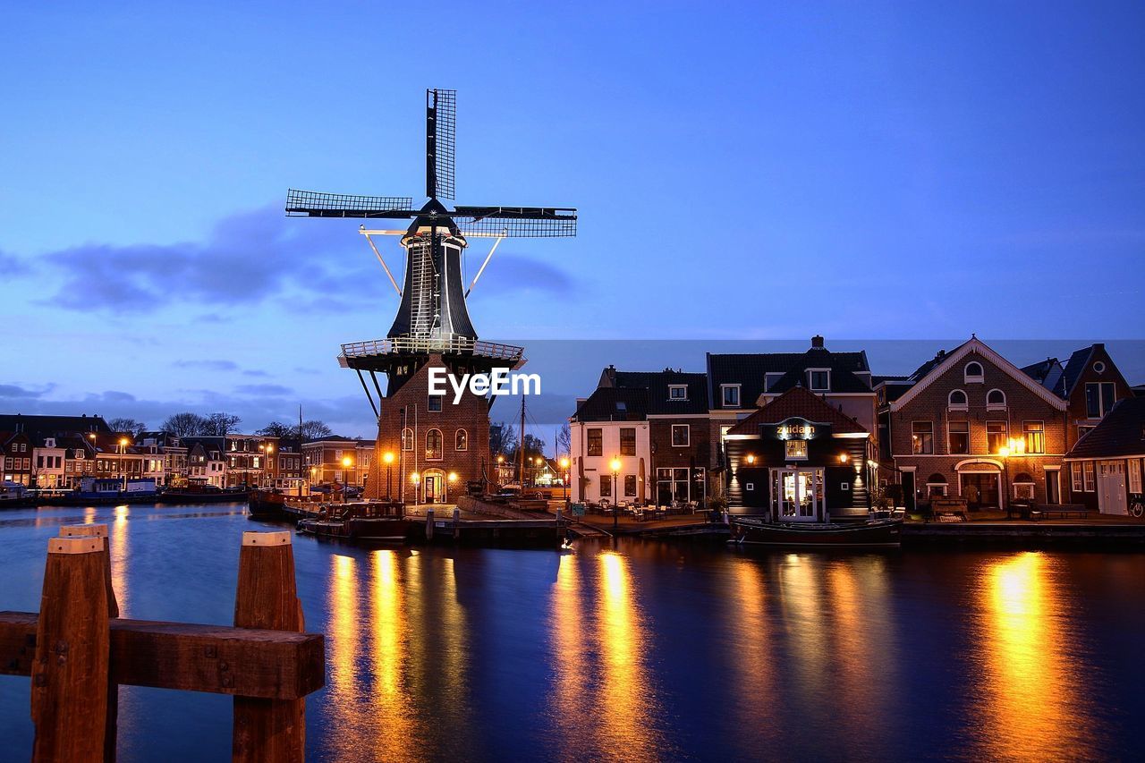 Traditional windmill amidst houses by lake at dusk