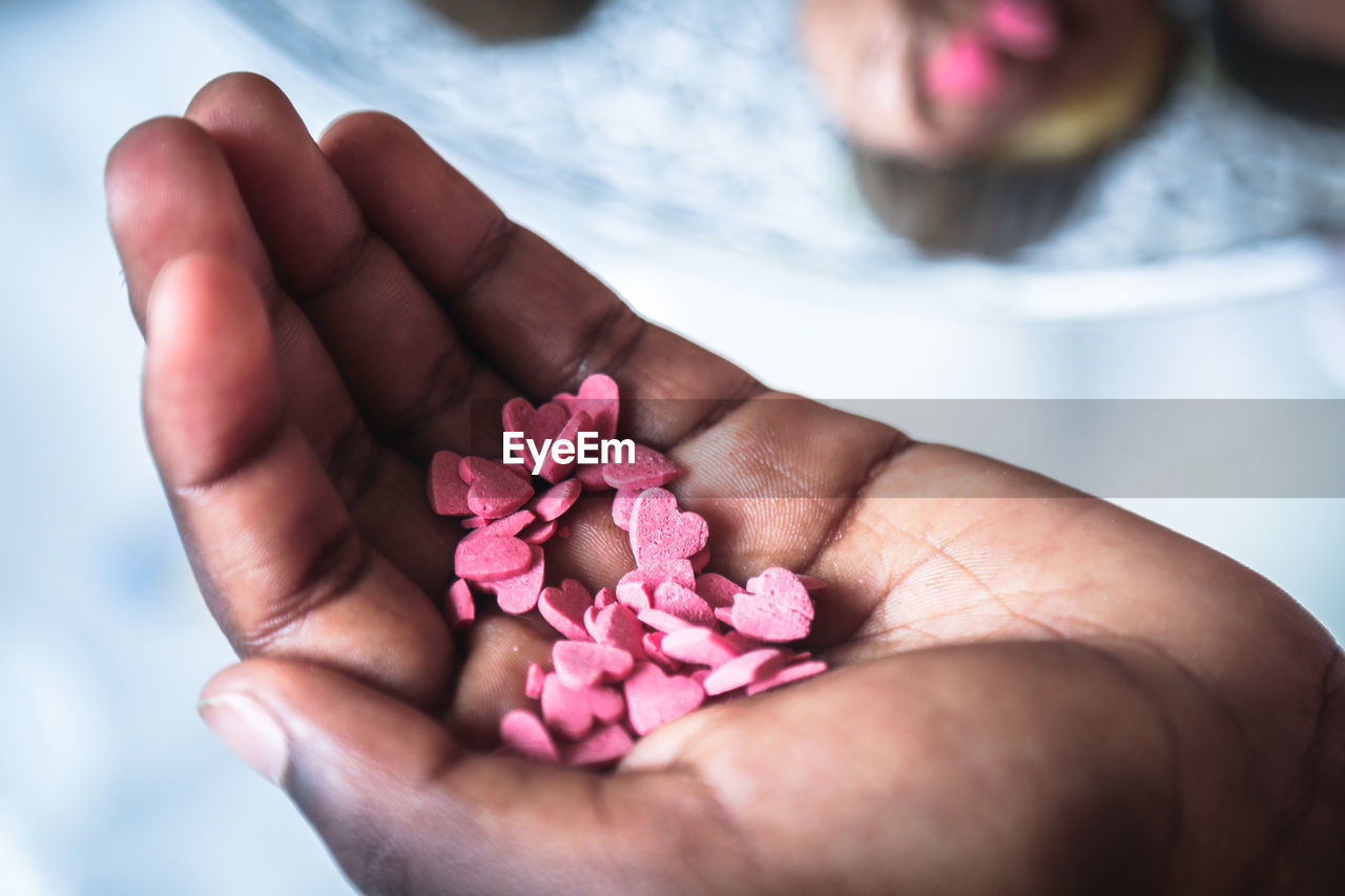 Cropped hand holding pink heart shaped candies over table