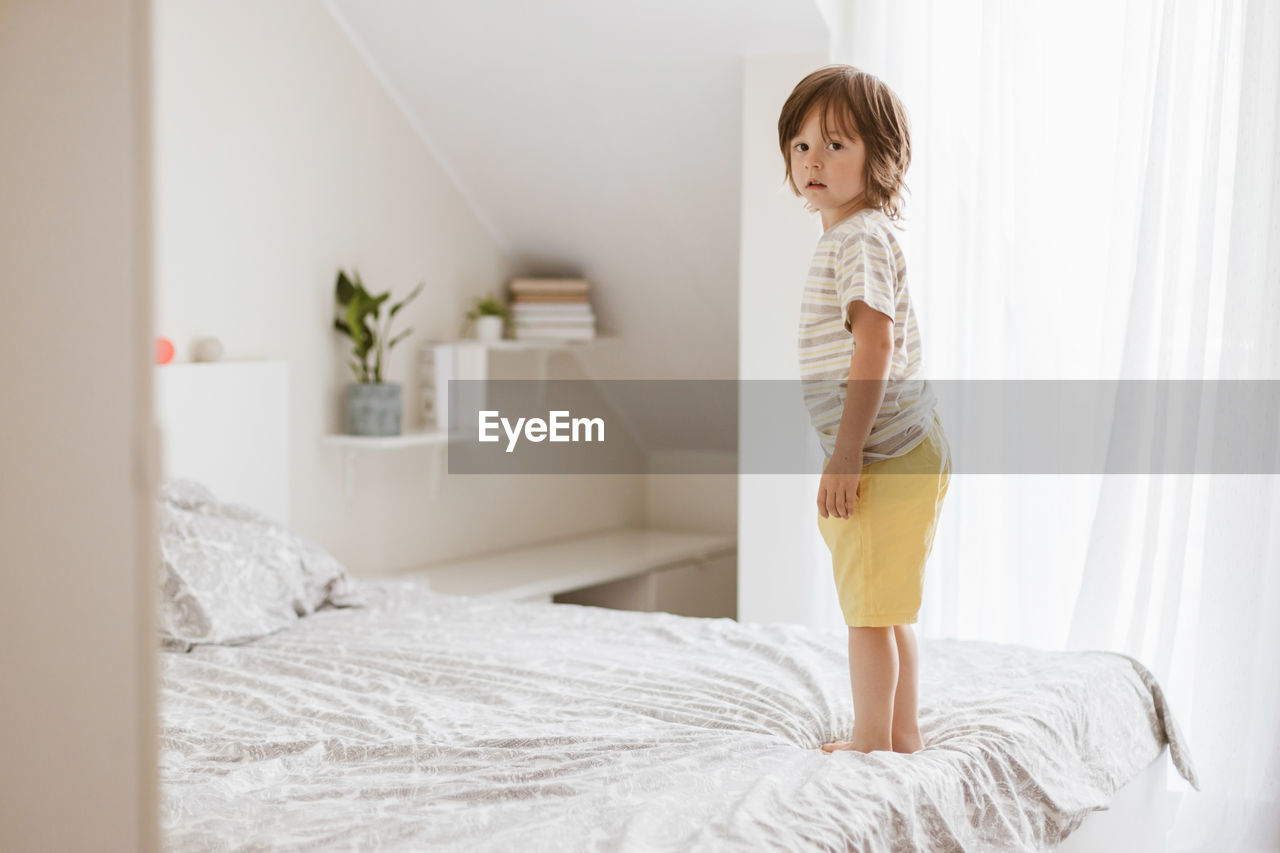 A little boy joyfully jumps on the bed in the bedroom. fun games at home. children's activity 