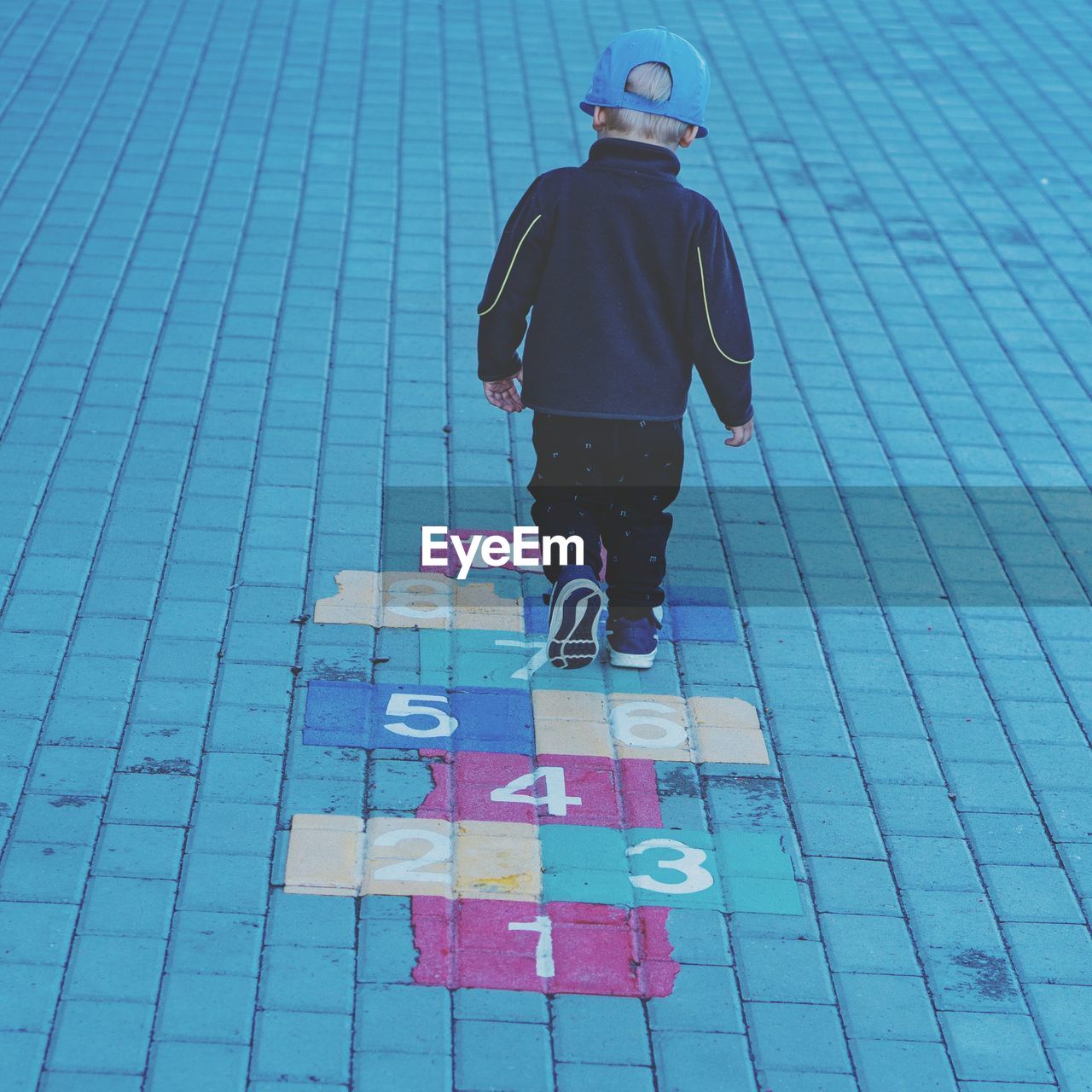 Rear view of boy playing hopscotch on footpath