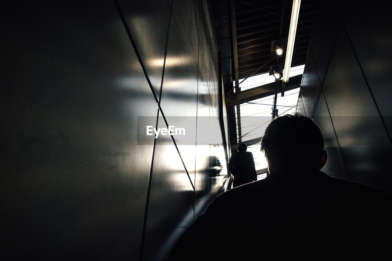 REAR VIEW OF SILHOUETTE MAN STANDING AGAINST SKY IN CORRIDOR