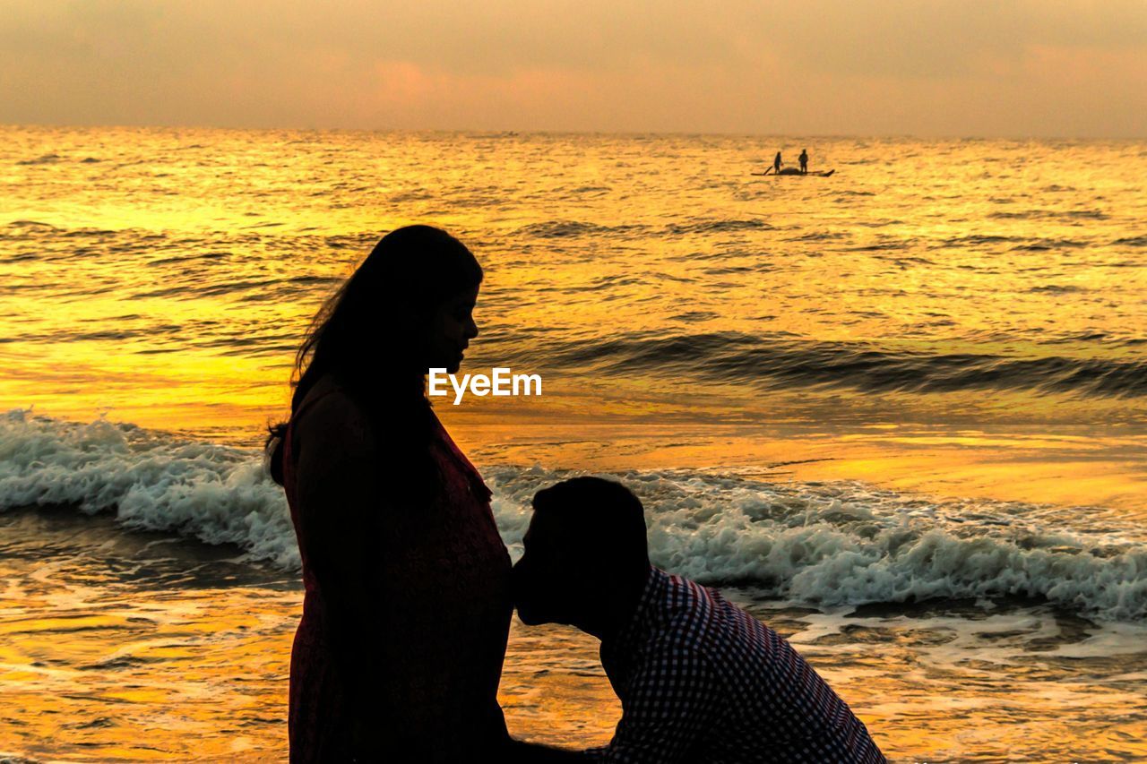 SILHOUETTE WOMAN LOOKING AT SEA SHORE AGAINST SKY DURING SUNSET