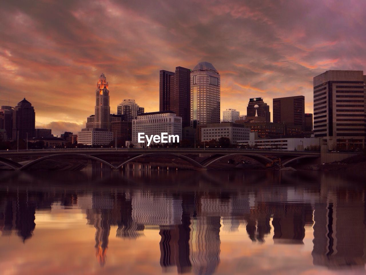 Reflection of cityscape on lake against cloudy sky at dusk