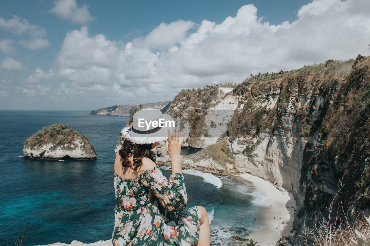 Woman standing on rock by sea against sky