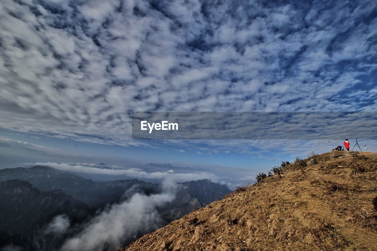 Distant view of man standing on mountain against sky