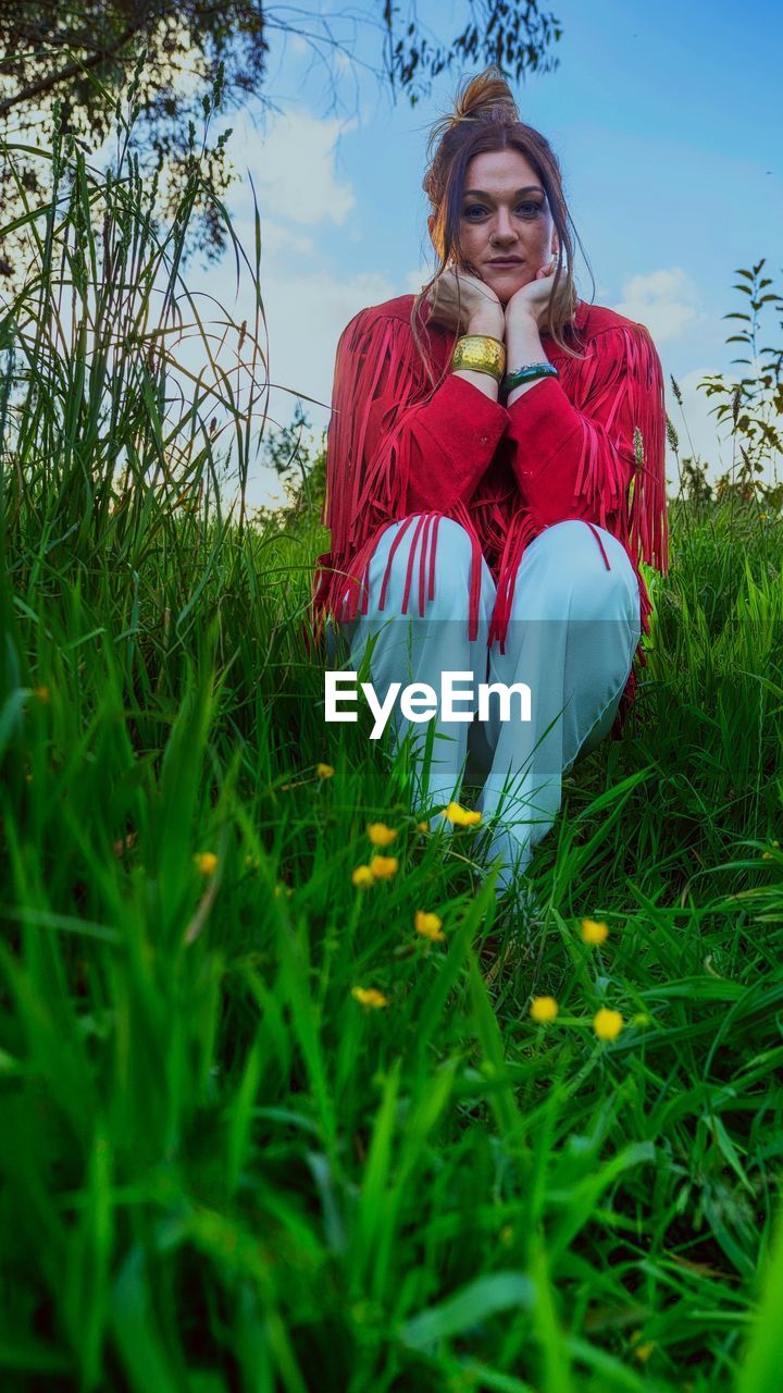 plant, flower, grass, one person, green, nature, meadow, women, adult, front view, sky, clothing, red, field, young adult, portrait, leisure activity, land, day, blond hair, outdoors, lifestyles, sunlight, emotion, smiling, looking at camera, sitting, beauty in nature, female, rural scene, three quarter length, long hair, person, hairstyle, happiness, plain, growth, looking, landscape