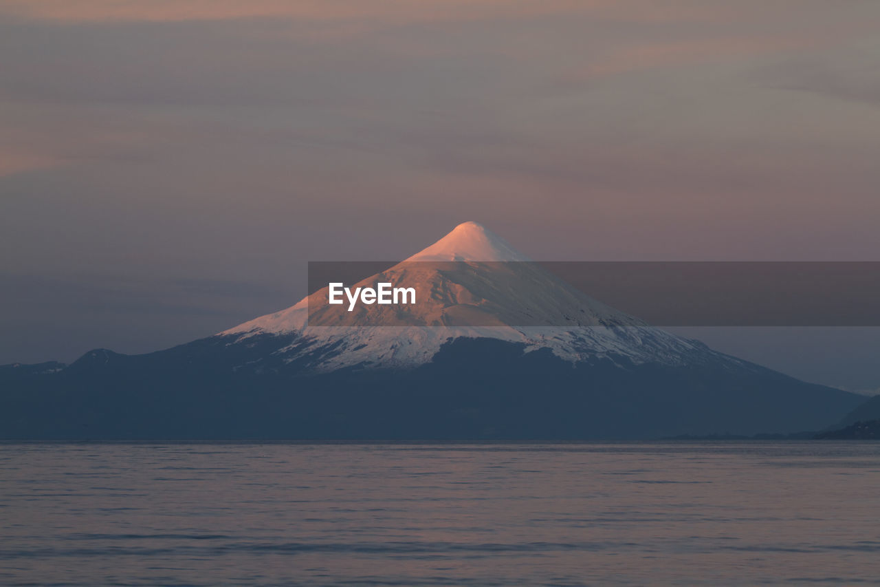 Scenic view of snowcapped mountains in front of sea during sunset