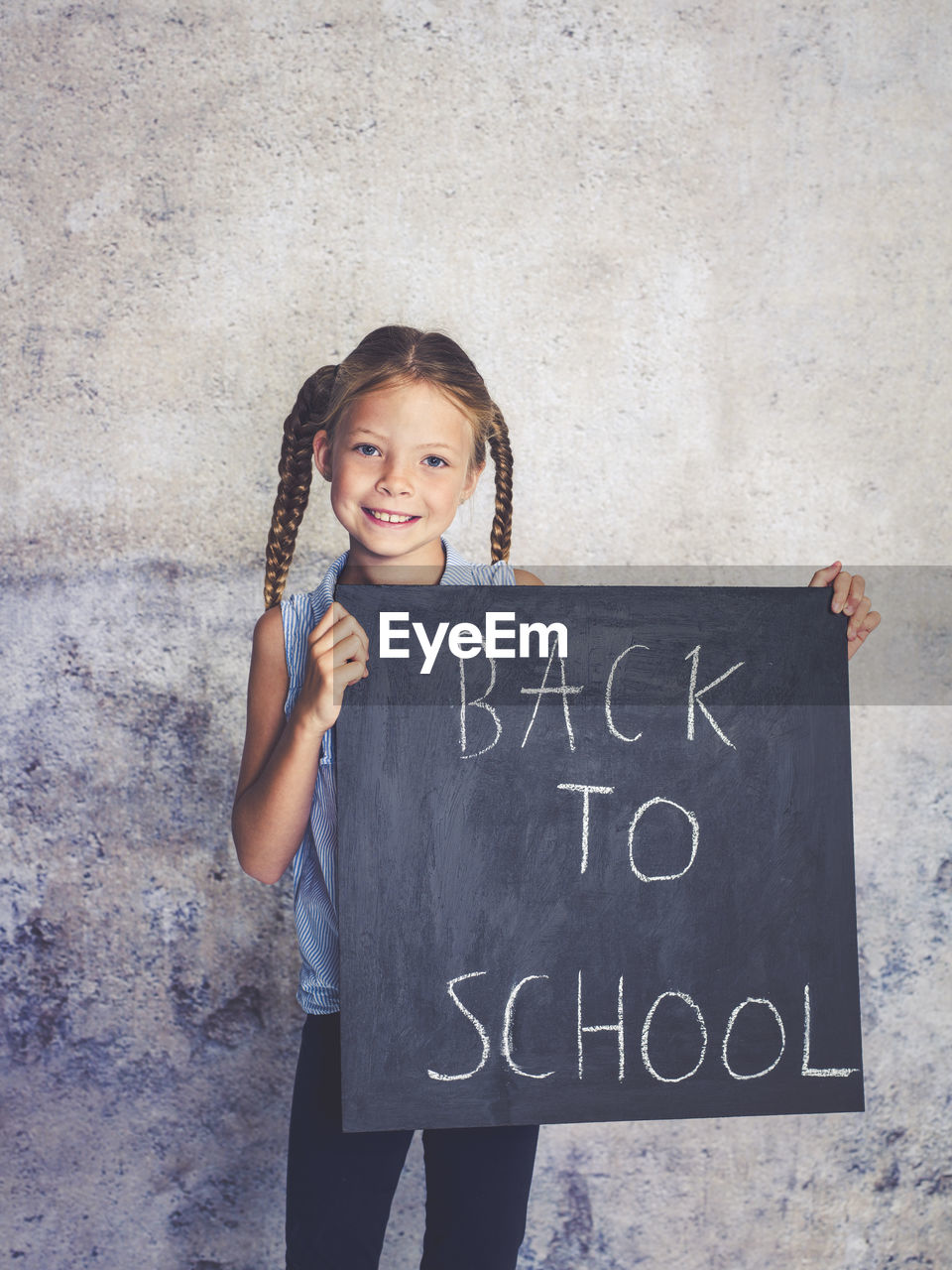 Portrait of smiling girl holding writing slate with text against wall