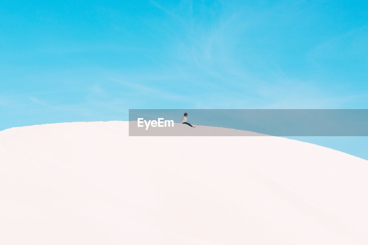 Low angle view of woman sitting on sand dune against clear sky