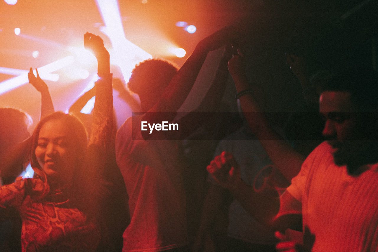 Happy young male and female friends enjoying dance at illuminated red nightclub