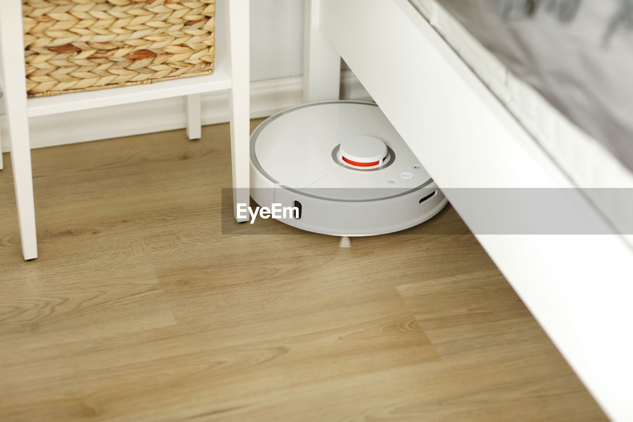 White robotic vacuum cleaner on laminate floor cleaning dust in living room interior. smart electron