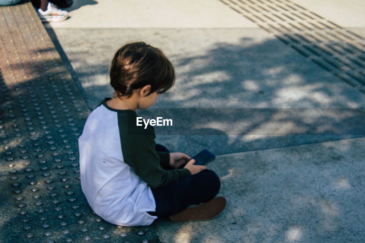 SIDE VIEW OF BOY SITTING OUTDOORS