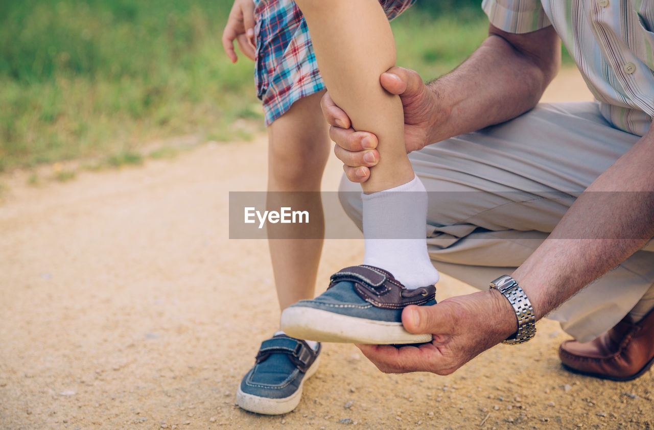 Low section of grandfather helping grandson to put on shoe