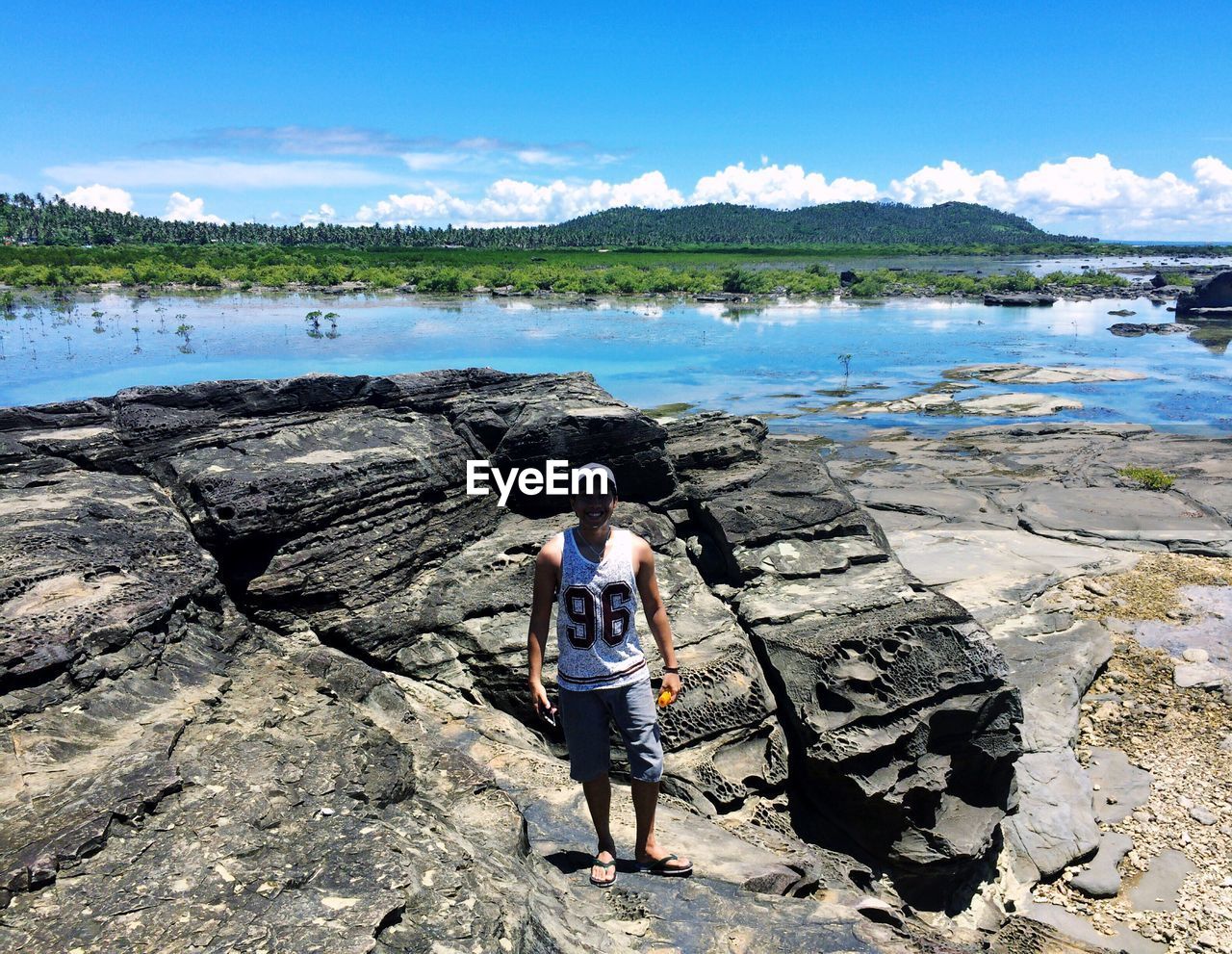 REAR VIEW OF WOMAN STANDING ON ROCK BY SEA AGAINST SKY