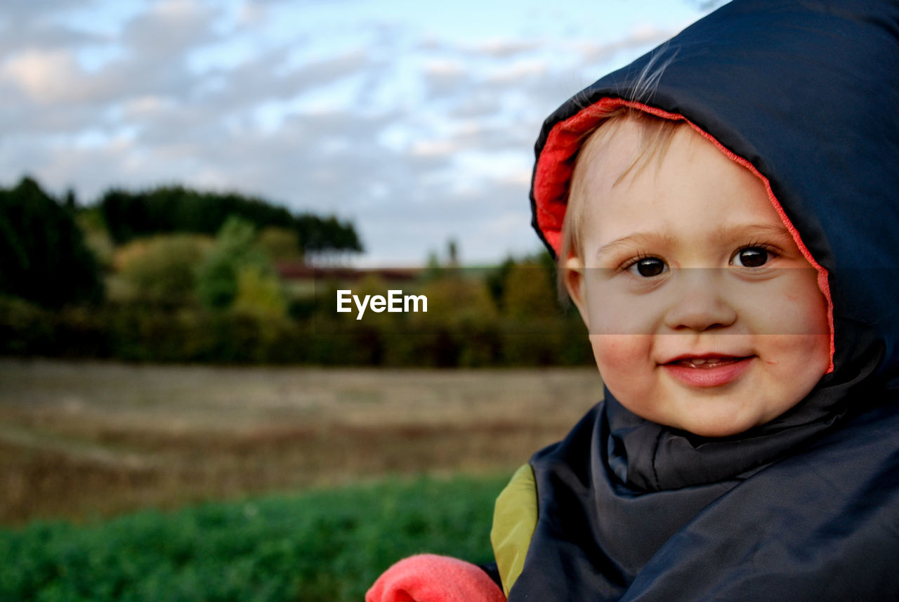 Close-up portrait of cute baby wearing hooded shirt at field