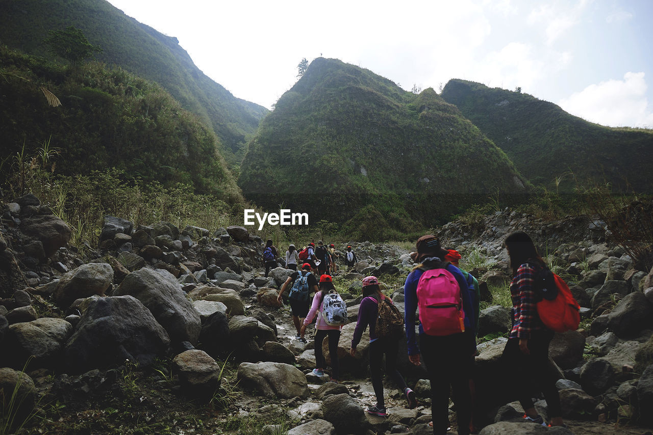 Rear view of people with backpack hiking against mountains