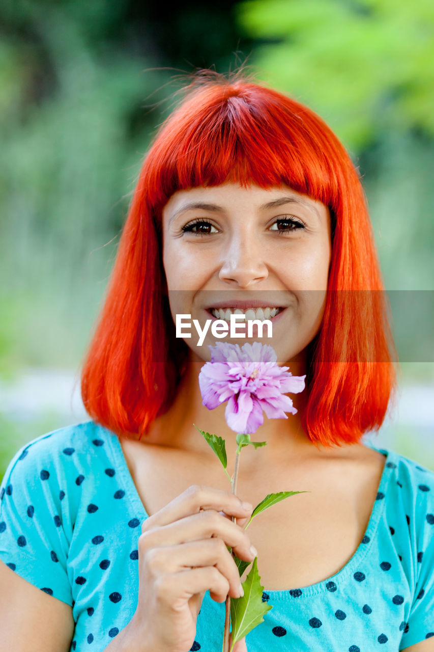 Close-up portrait of smiling woman with redhead holding flower