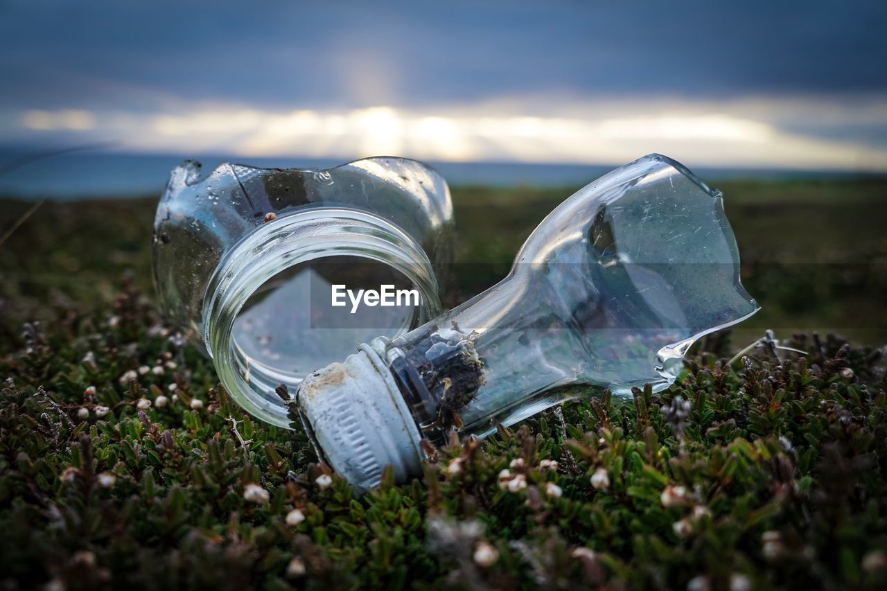 CLOSE-UP OF GLASS OF BOTTLE ON FIELD