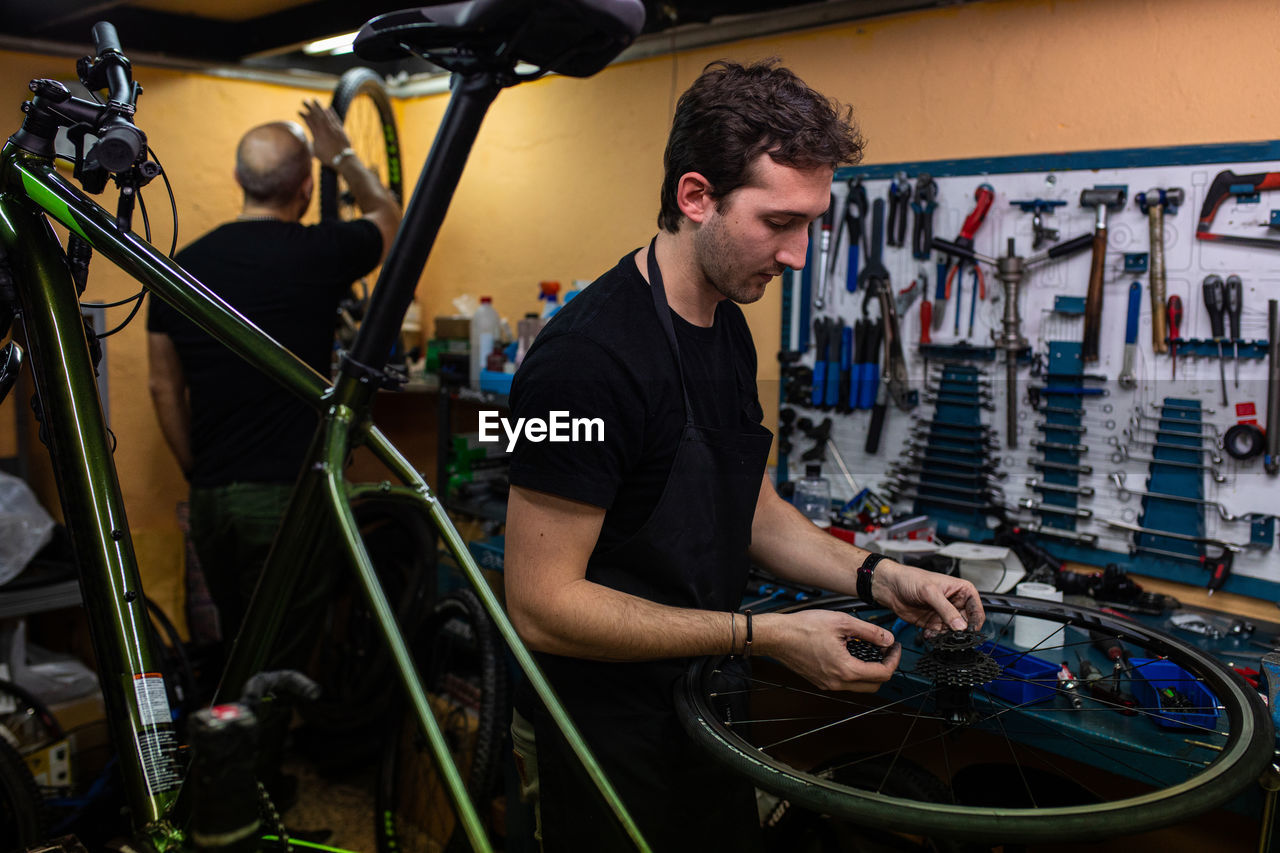 Technician with dirty hands fixing bicycle wheel while working in workshop