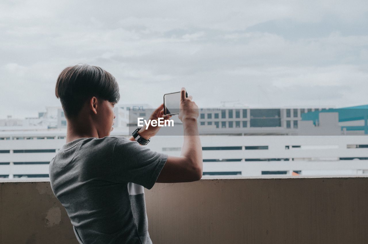 Man photographing with mobile phone against sky