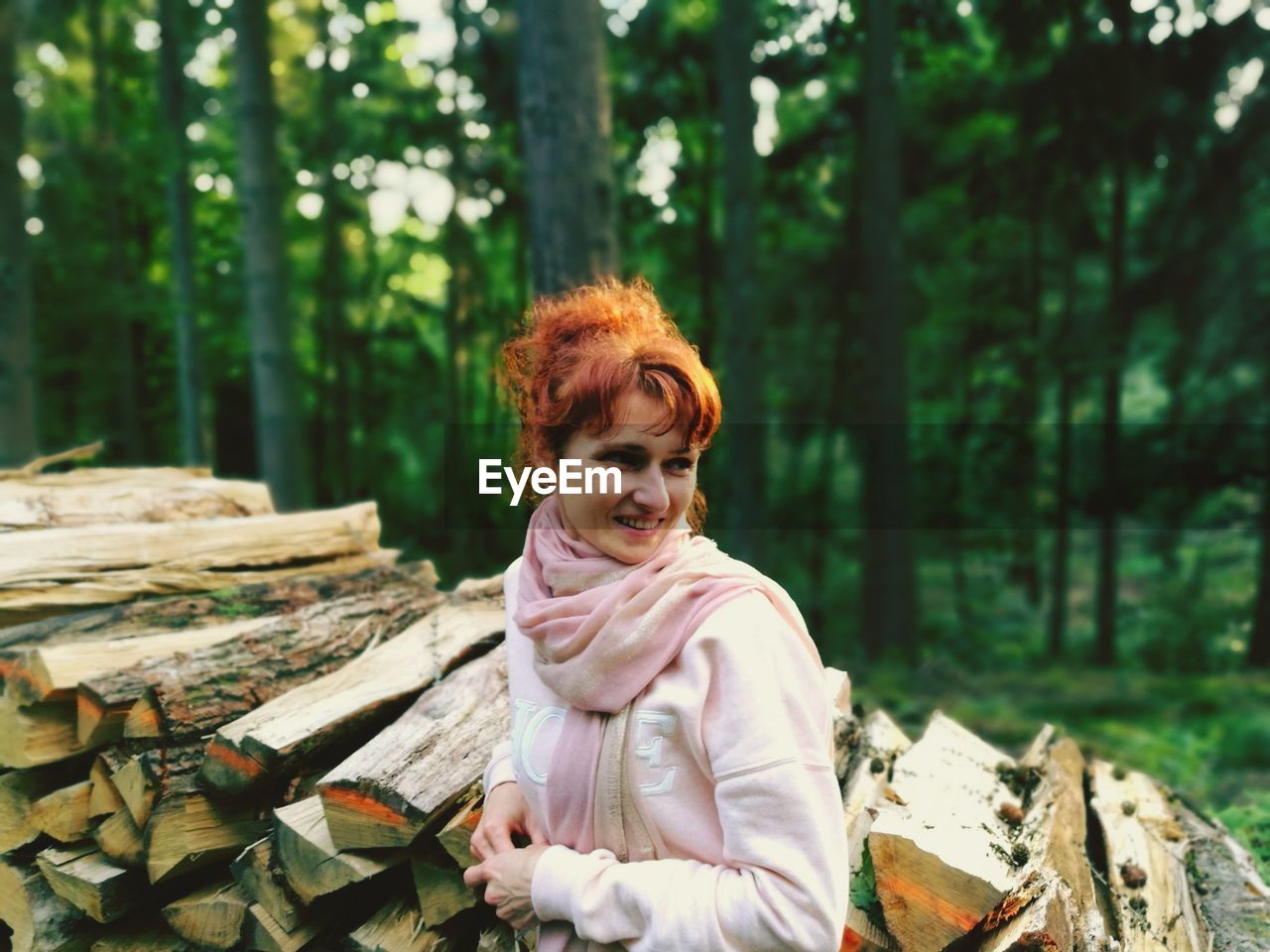 Woman looking away while standing against trees in forest