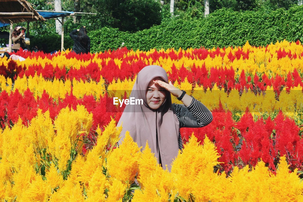 Portrait of smiling young woman standing by yellow flowering plants