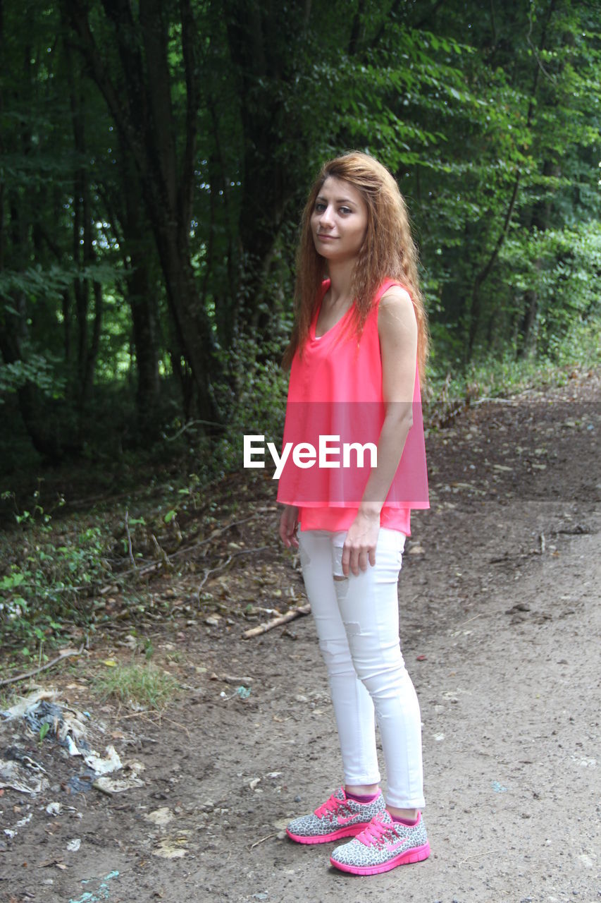 PORTRAIT OF A YOUNG WOMAN SITTING ON TREE TRUNK