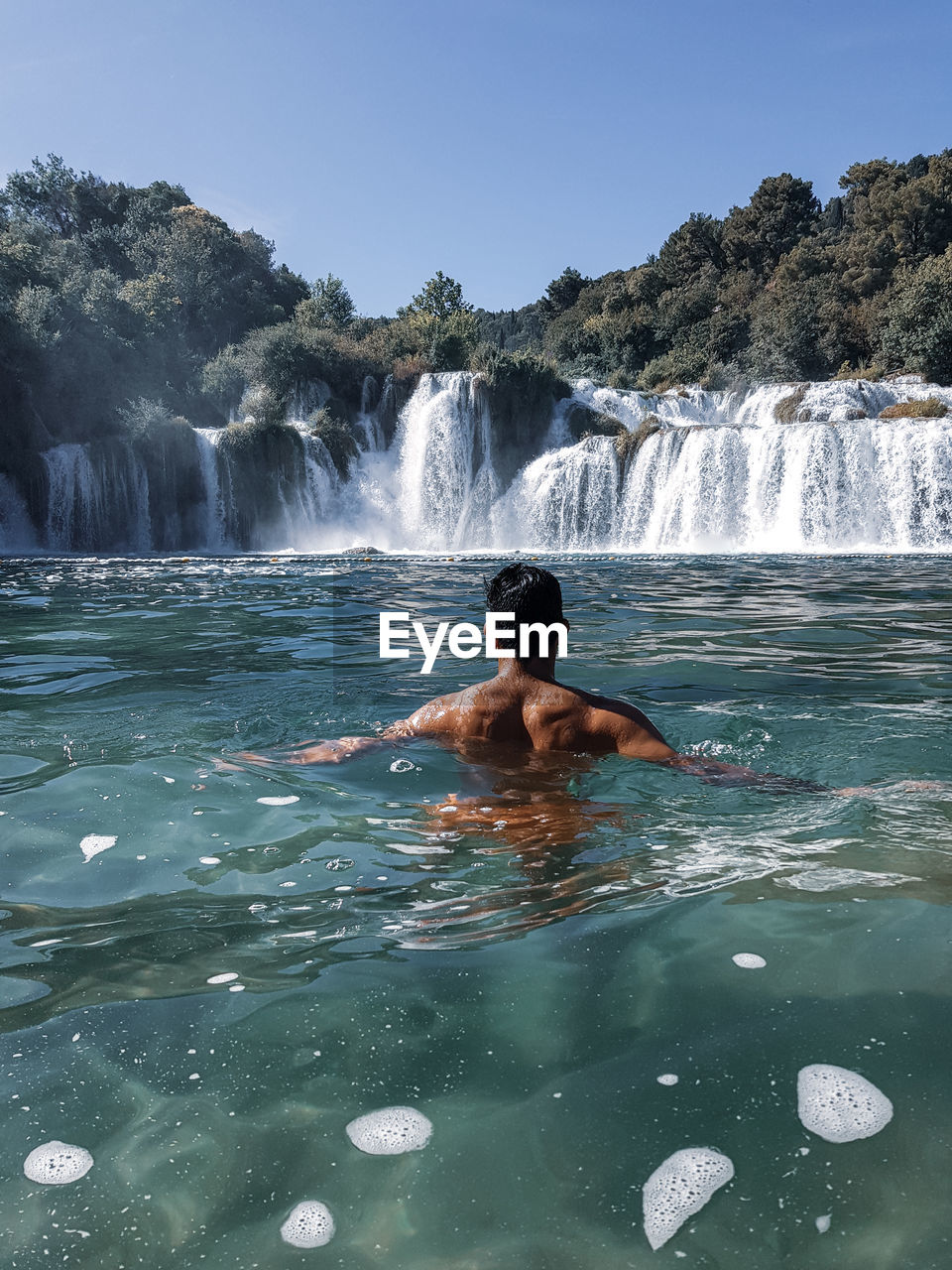 Rear view of shirtless man against waterfall in river