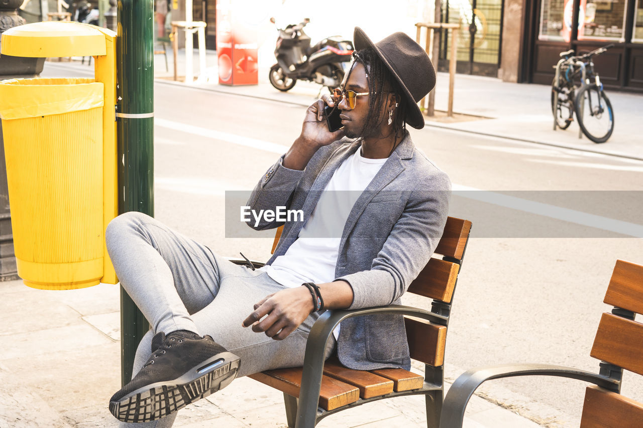 Young man talking on phone while sitting by road at chair