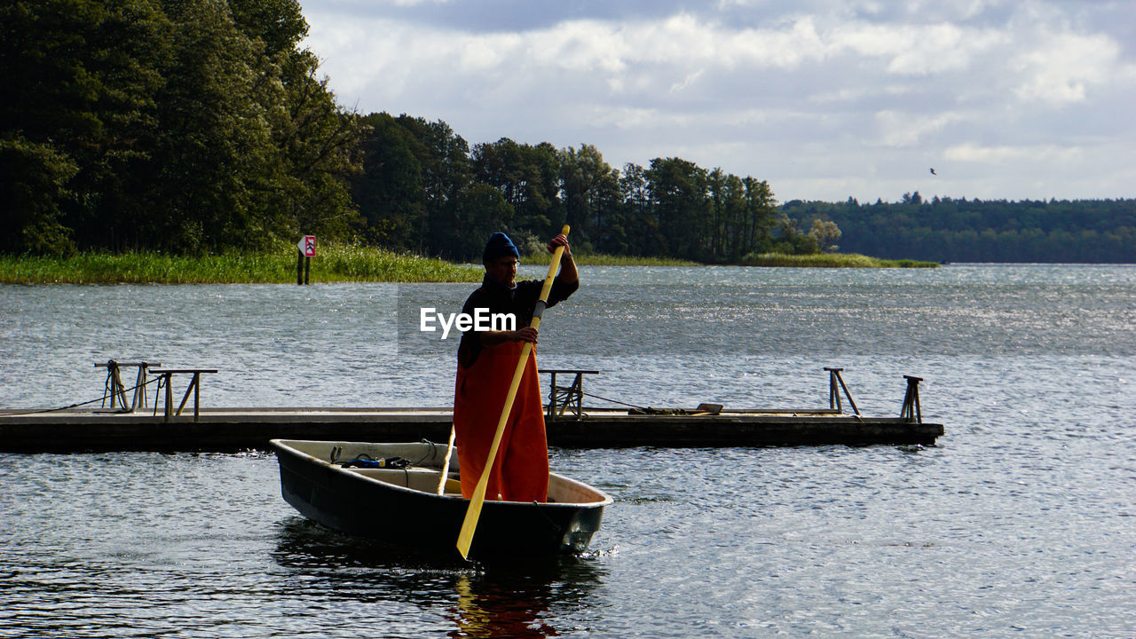 Man standing on boat in lake against sky