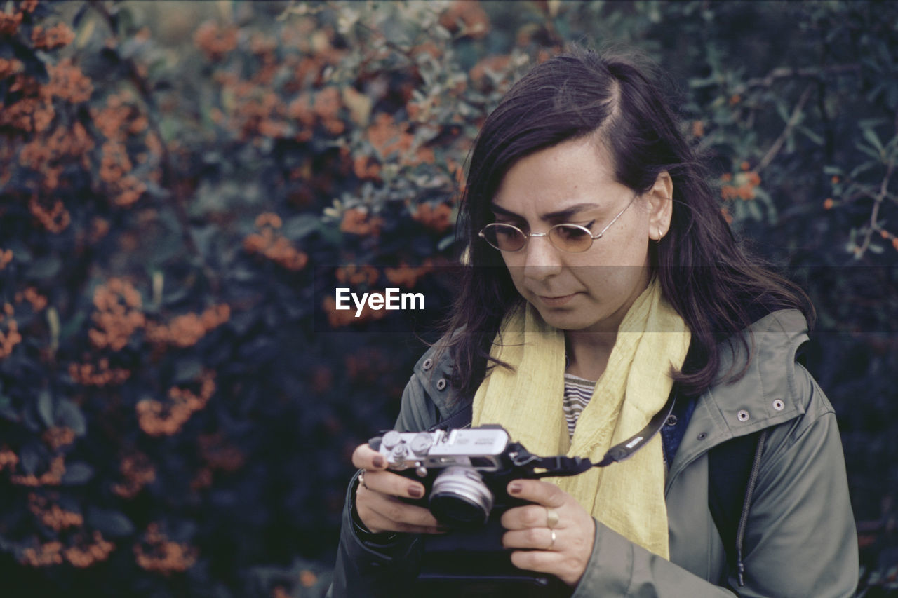 Close-up of woman holding camera against trees in forest