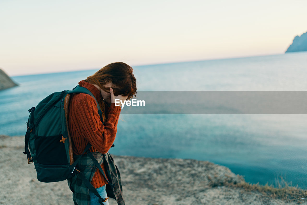 Woman with head in hand standing near sea