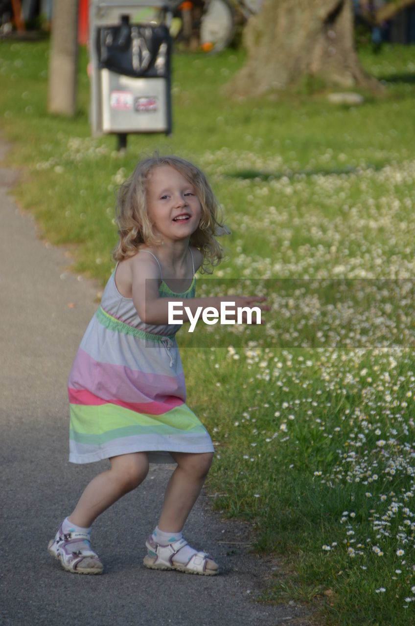 Full length of girl standing on road by grassy field