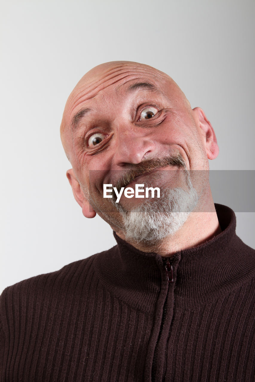 Close-up portrait of happy mature man making face against gray background