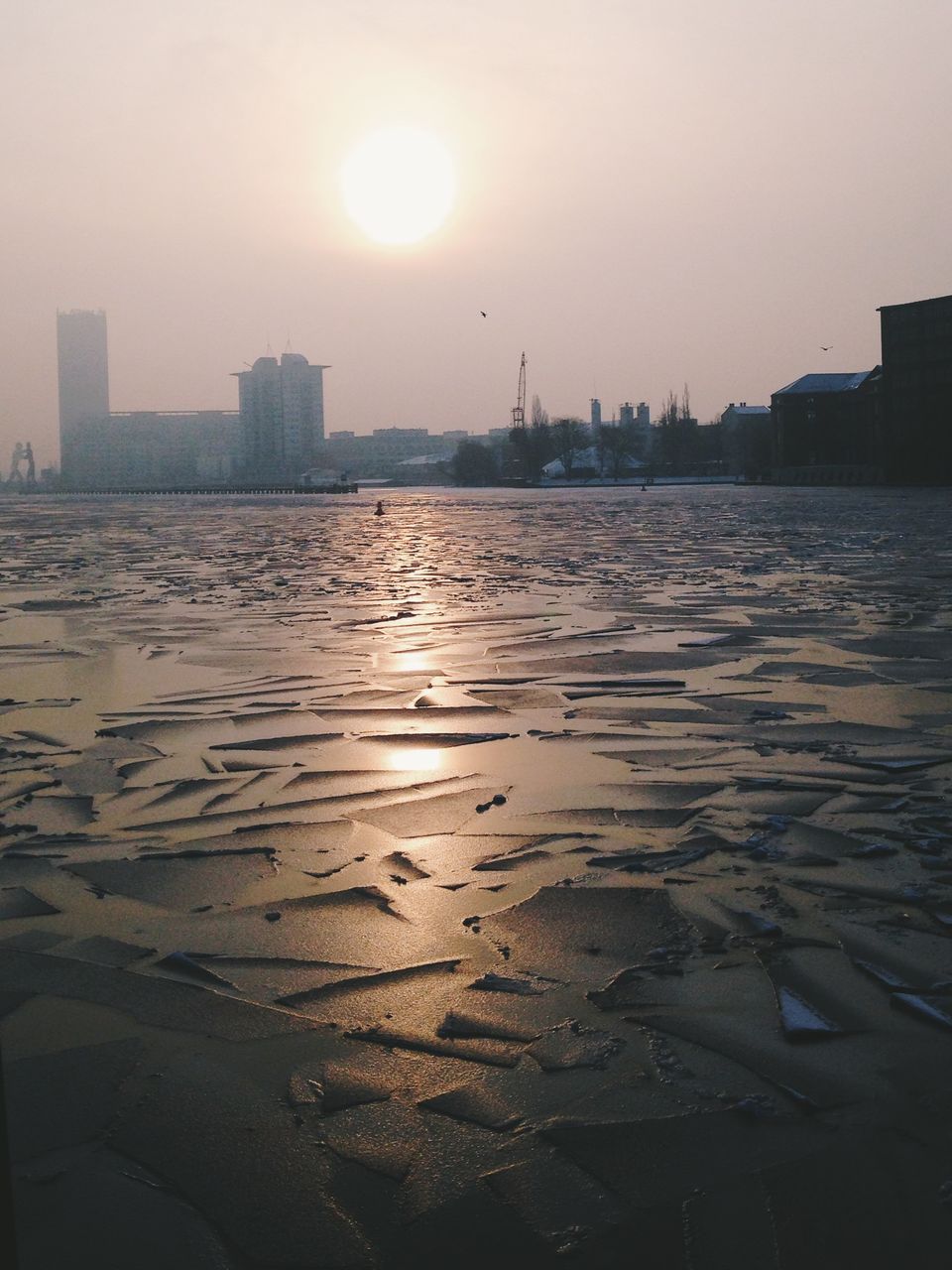 Frozen river in city at sunset
