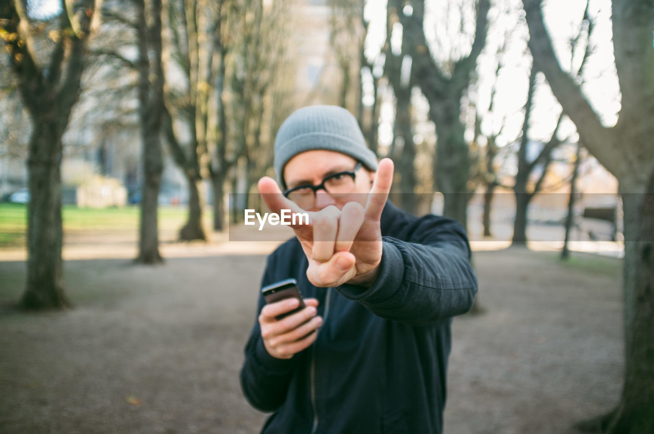 Portrait of mid adult man showing rock sign in park